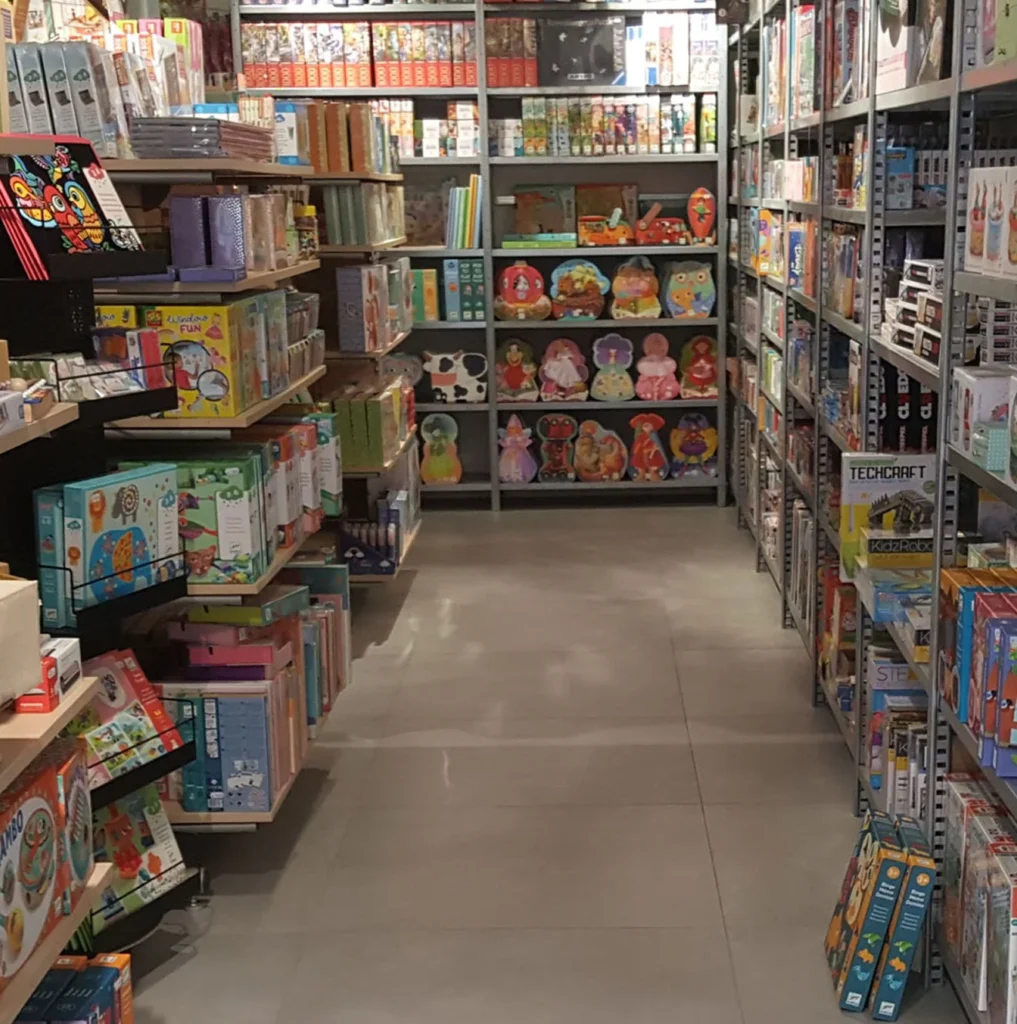 Gangpad in een winkel met planken vol kleurrijke spellen en speelgoed.