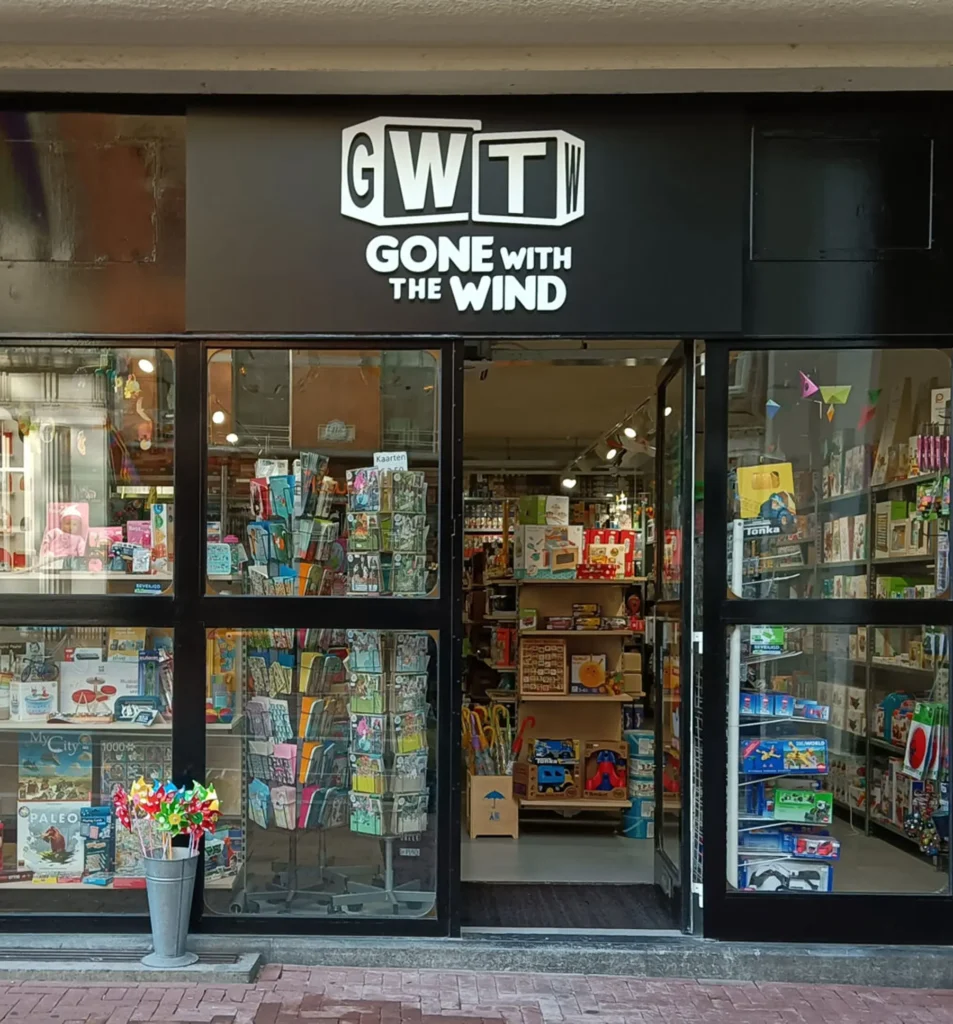 Voorkant van een winkel genaamd "GWT Gone With The Wind," met een open deur en spellen en kaarten in de etalage.